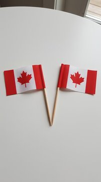 Two Canadian flags on a white desk surface.