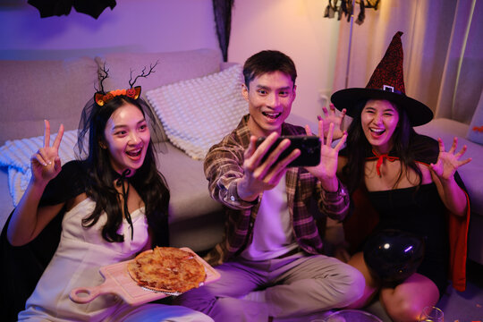 Young Asian friends taking a smartphone selfie with pizza at a Halloween party.