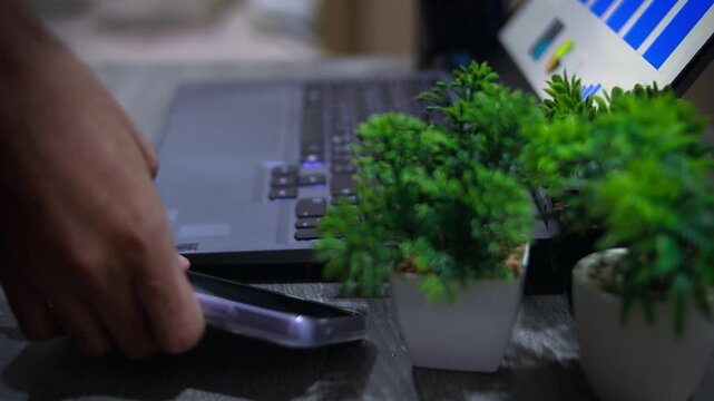Close up of businessman charging smartphone on office desk, representing remote work and home office lifestyle.