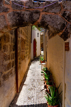 Rhodes, Greece - 16 May 2026: View of the narrow cobblestone alleyway in the historic Old Town of Rhodes, framed by stone arches and lined with potted aloe vera plants.