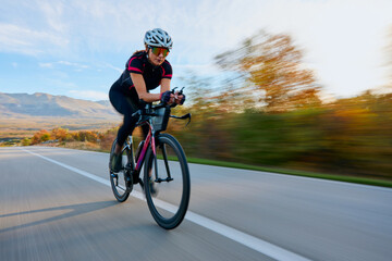 Naklejka premium Female Cyclist Road Cycling at Speed on Open Road With Autumn Landscape and Mountains