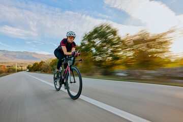 Fototapeta premium Female Cyclist Road Training At Speed Through Countryside On Racing Bike With Aerodynamic Gear