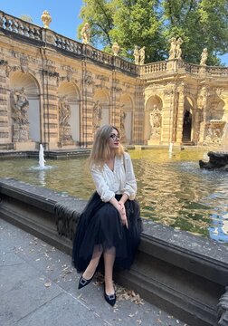 Elegant woman sitting by the fountain in courtyard at Zwinger Palace in Dresden, relaxing during summer vacation in Saxony, Germany 