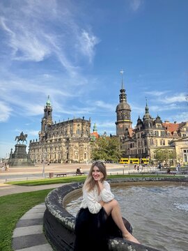 Elegant woman sitting by the fountain in courtyard at Zwinger Palace in Dresden, relaxing during summer vacation in Saxony, Germany 