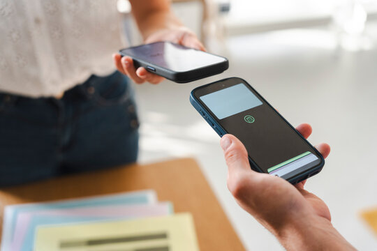 Two people use mobile phones to complete a secure contactless digital transaction. This technology allows for quick wireless data sharing between two handheld devices.