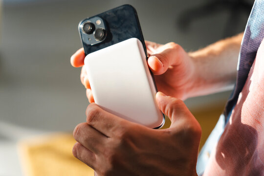 A person holds a dark smartphone in their hands while attaching a compact white magnetic portable power bank to the back for wireless charging while on the move.