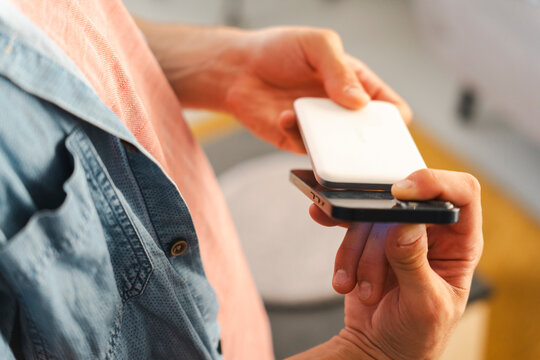 A man holds a modern smartphone while placing a white portable battery pack on top of it to charge the device wirelessly. This demonstrates convenient technology.