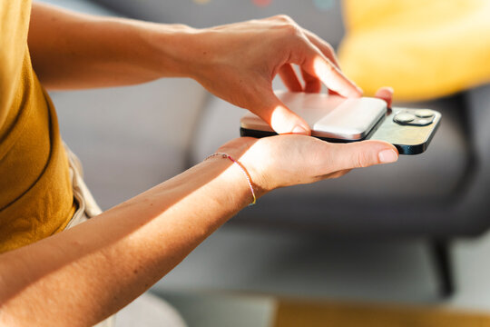 A woman attaches a portable power bank to the back of her smartphone to charge the battery while on the go. This convenient wireless accessory saves space.