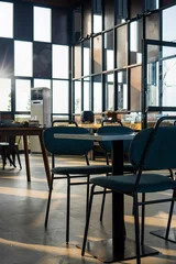 Fotobehang Horeca Modern restaurant interior illuminated by warm morning sunlight through large windows, featuring dining tables, chairs, and architectural details.  © ANTONIUS