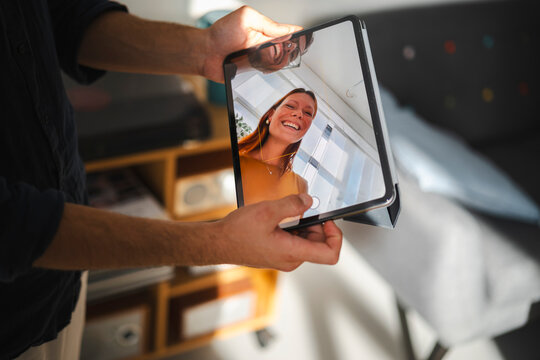A person holds a digital tablet to record a video of a woman with red hair. The screen shows the frame interface while the photographer is visible in the reflection.