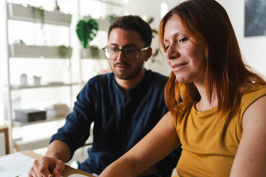 A young woman and a man work together in a bright office space. They focus on a creative project on their table, collaborating effectively on their shared task.