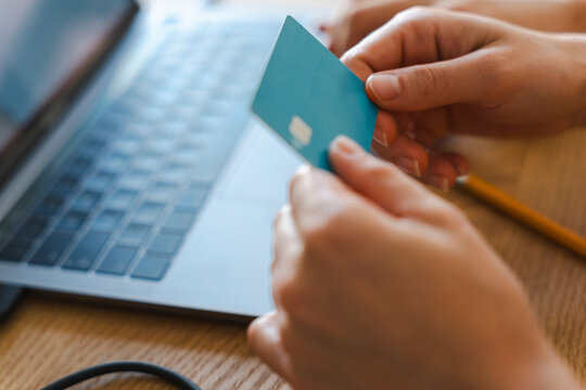 A person holds a bank card in their hands while sitting in front of an open laptop. They are making an online purchase or managing their finances from home today.