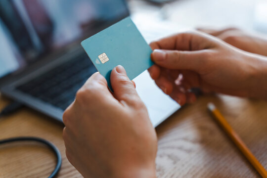 A person holds a payment card while sitting at a desk with a laptop. They are ready to input financial information to complete a secure online purchase transaction.