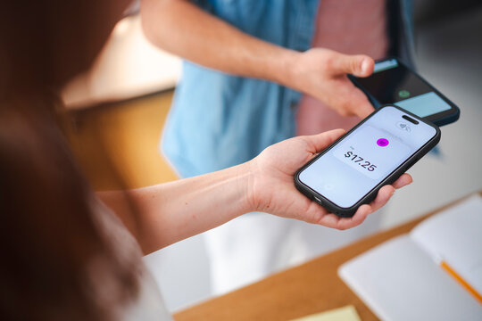 A customer uses a smartphone to complete a contactless payment at a store. The cashier holds a mobile device to facilitate the retail transaction for seventeen dollars.
