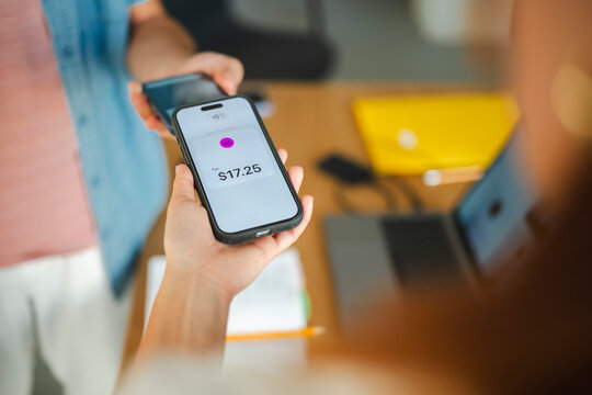 A customer makes a contactless payment of seventeen dollars and twenty-five cents using a smartphone held over a merchant device in a modern office or store environment.