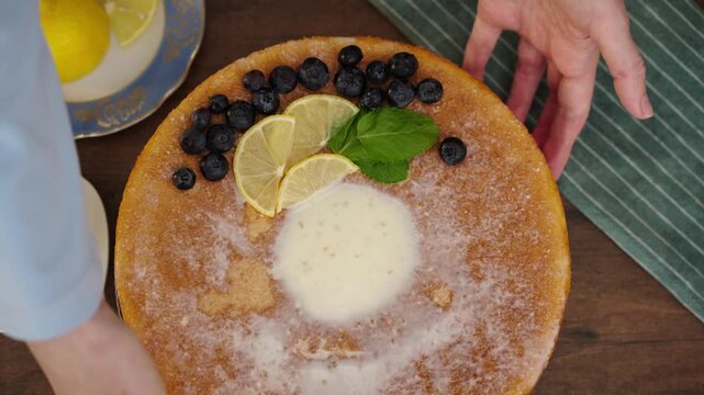 Hand presenting finished lemon blueberry cake in cozy kitchen
