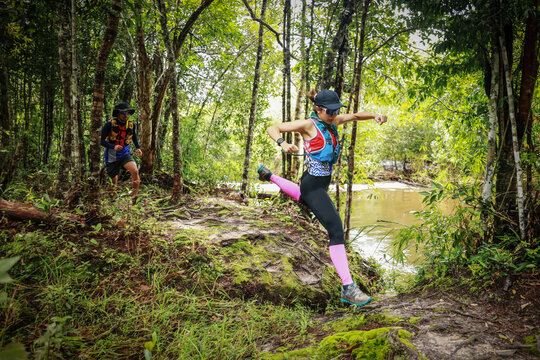 Trail runners navigating a rugged forest path beside a river, showcasing outdoor adventure, fitness, endurance, and connection with nature