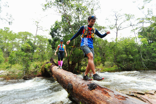 Trail Runners Crossing a Fallen Tree Over a Fast Flowing River in the Forest