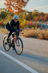 Fototapeta premium Female Cyclist Training on Road Bike During Autumn Sunrise Outdoors Wearing Helmet and Sunglasses
