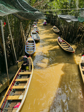 Vietnam - 17 August 2026: View of traditional wooden boats navigating a narrow canal in the Mekong Delta, with local people wearing conical hats under the shade of lush palm trees.