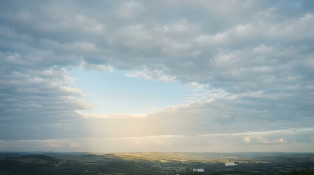 Expansive Cloudy Sky Over Rolling Hills and Distant River at Sunrise clouds dawn