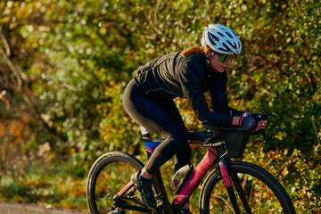 Fototapeta premium Female Cyclist Training on Road Bike in Autumn Countryside Wearing Helmet and Sunglasses