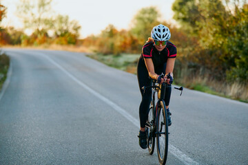 Naklejka premium Female Road Cyclist Training on Country Road at Sunrise Showing Fitness, Focus and Endurance