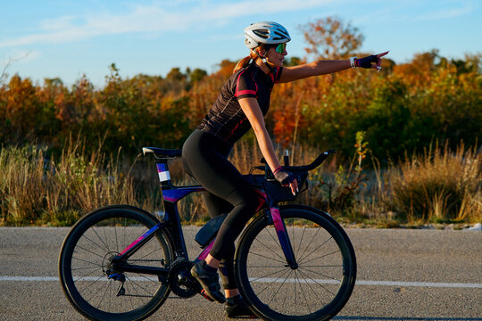 Female Cyclist On Road Bike Pointing Ahead During Autumn Outdoor Training At Sunset