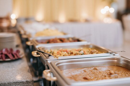 Hotel banquet buffet line with polished steel chafing trays of rich curries and rice, featuring warm golden lighting for catering and wedding service