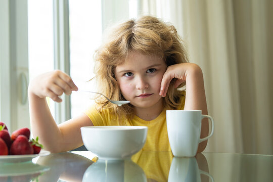 Bored Child Holding Spoon at Breakfast Table. Child holding a spoon and resting their head on one hand during breakfast at home. Portrait of a bored picky eater sitting beside a bowl, cup