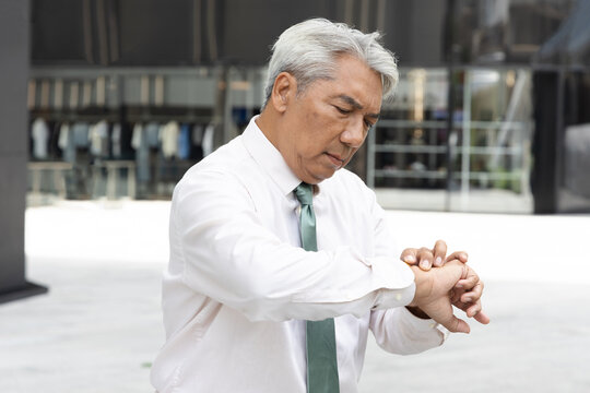 asian senior businessman looking at his wristwatch outdoors in the city, stressed about running late for an appointment