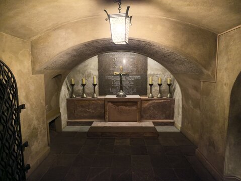 Vilnius, Lithuania - 22 July 2026: View of the historic crypt inside Vilnius Cathedral, featuring a stone altar, a central cross, and lit candles under a vaulted ceiling.
