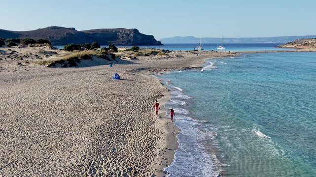 Discover the tranquility of Simos Beach, where calm turquoise waters meet soft sands. Enjoy a peaceful walk by the shoreline under the clear blue sky, ideal for relaxation.