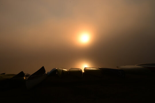 Misty morning sunrise over canoes on the beach at Lake of Two Rivers Campground in Algonquin Provincial Park Ontario Canada 