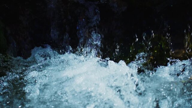 Water crashes down dark rocks. Bubbles and spray rise with force. Light glints on wet surfaces. Nature's raw energy captured in motion. Perfect for adventure or environmental themes