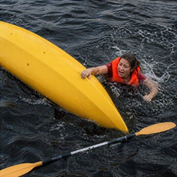 Woman struggling in water beside overturned kayak after boating accident