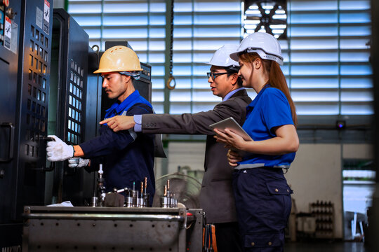 Asian factory manager and engineer team inspecting machine components with digital tablet in plant	
