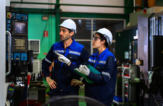 Factory workers reviewing clipboard checklist near industrial machinery in manufacturing plant. ideal for industrial quality control, team engineering, and manufacturing concepts.