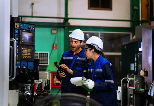 Factory workers reviewing clipboard checklist near industrial machinery in manufacturing plant. ideal for industrial quality control, team engineering, and manufacturing concepts.