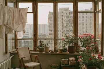 Fototapeta premium Retro home interior with a wide wooden window overlooking apartment blocks, flowering plants and soft natural light for a peaceful nostalgic mood.