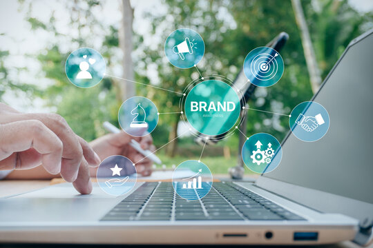 Business professional working on laptop with holographic brand awareness and marketing strategy network icons, concept of corporate identity, public relations, and business growth.