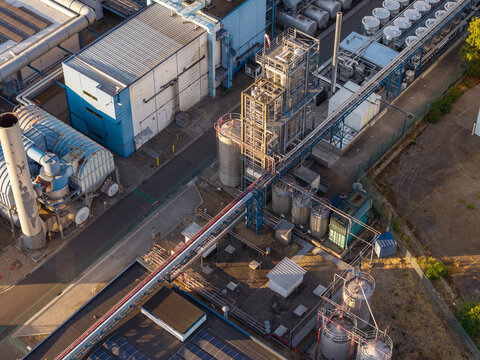 Aerial view of an industrial chemical plant featuring complex pipe networks, storage tanks, and manufacturing facilities in Genk, Flanders, Belgium.
