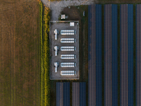 Aerial view of a solar farm featuring rows of photovoltaic panels and a central battery energy storage system enclosure situated in a rural landscape in the Netherlands.