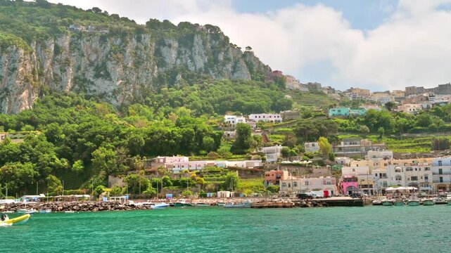 Scenic coastal landscape of capri island showing rugged cliffs and marina with moving yellow boat in mediterranean sea.