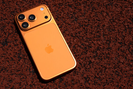 KYIV, UKRAINE - July 10, 2026 : Apple iPhone 17 Pro in Cosmic Orange color on red sport field with artificial rubber surface.