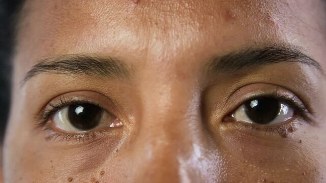 Portrait of young Hispanic woman looking directly into camera and blinking in extreme close up. Footage is ideal for ophthalmology, contact lens advertising, or skincare marketing campaigns