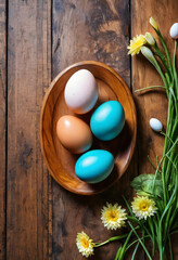 Fototapeta premium Easter celebration and spring holiday concept, colorful dyed eggs in a wooden bowl with fresh flowers on rustic wood background