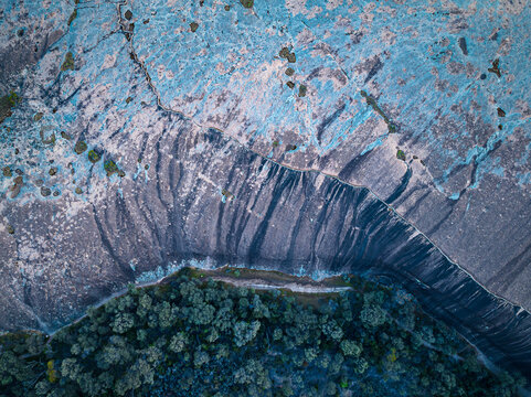 Aerial view of Wave Rock showing its distinctive curved granite cliff face with vertical streaks and surrounding native bushland in Hyden, Western Australia, Australia.