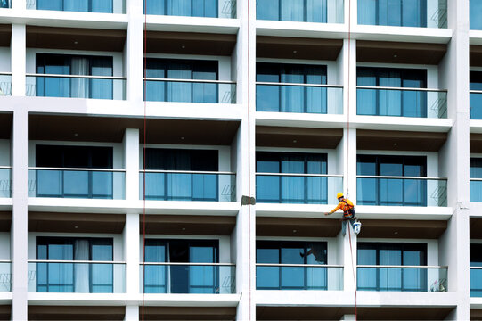Industrial painter in safety gear working on high rise building facade. Industrial climber servicing high rise