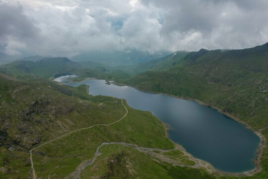 Aerial view of Llyn Llydaw in Eryri National Park surrounded by rugged green mountain slopes and dramatic cloudy skies in Wales, United Kingdom.